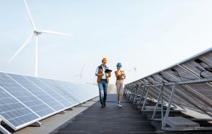 View on the rooftop solar power plant with two engineers walking and examining photovoltaic panels. Concept of alternative energy and its service